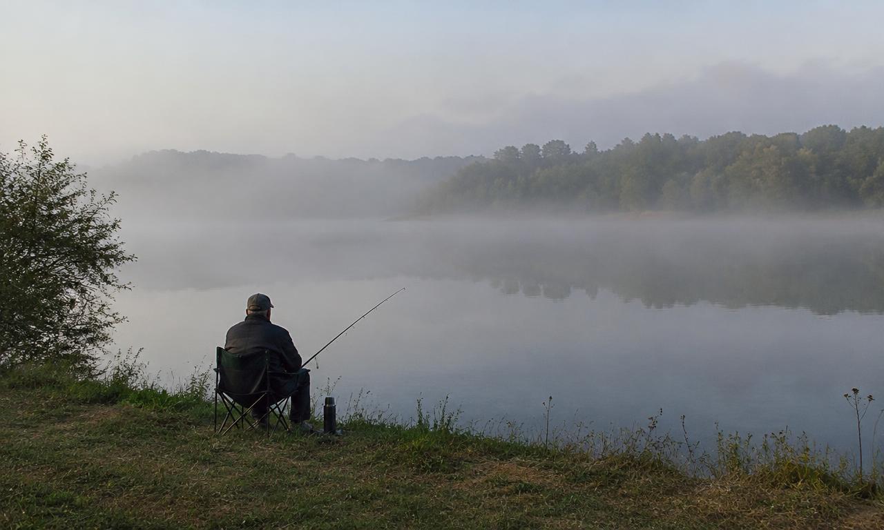 Homme pêchant au bord d'un lac brumeux au lever du jour